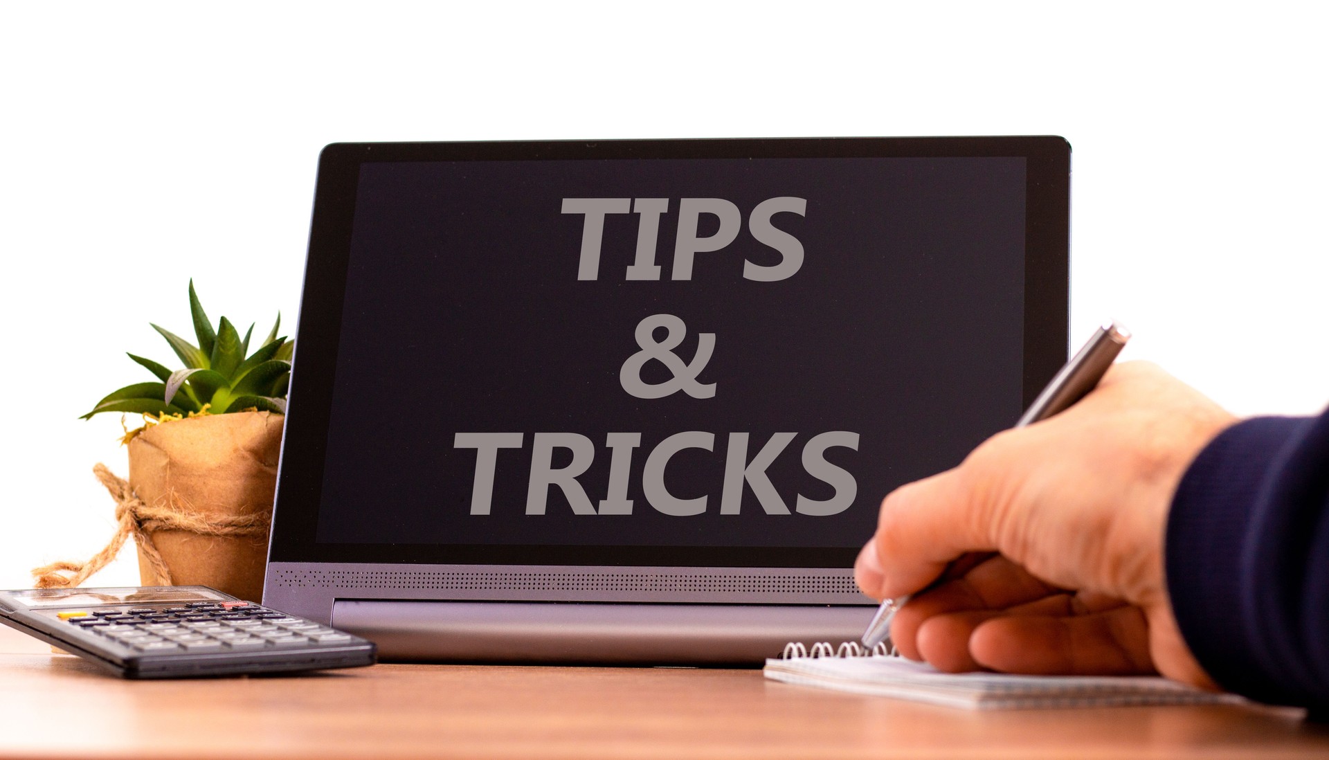 Tips and tricks symbol. Tablet with words 'Tips and tricks'. Businessman hand with pen, house plant. Beautiful white background. Business, tips and tricks concept, copy space.